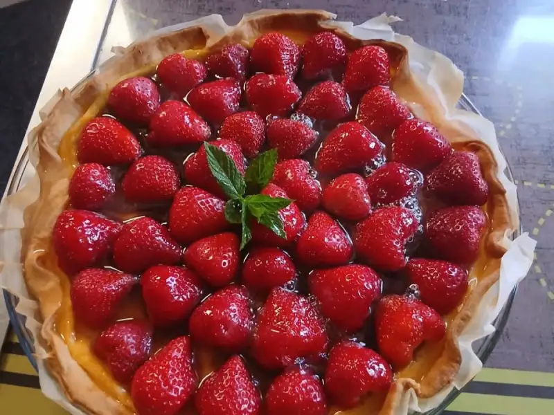 Huisgemaakte aardbeientaart met hele aardbeien op banketbakkersroom, versierd met munt, in een glazen vorm