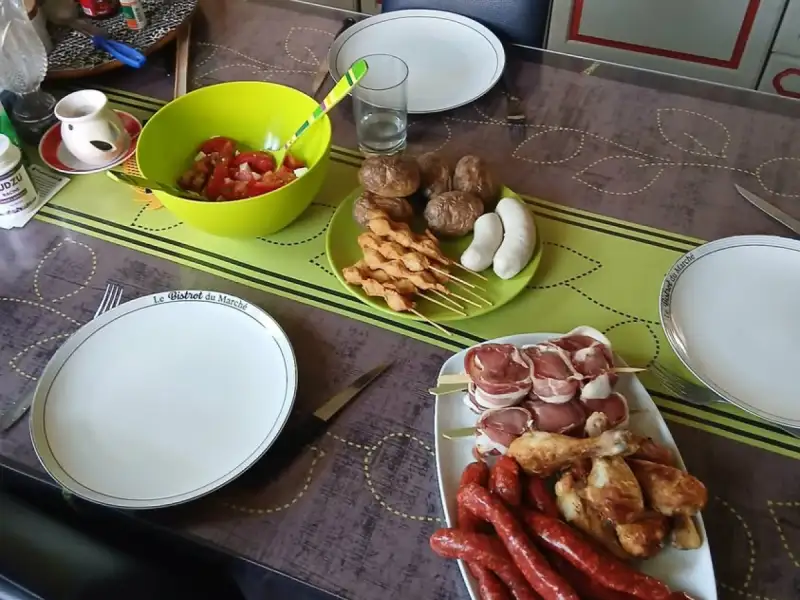 Rauwe kippenbrochettes op een barbecuetafel met worsten, drumsticks, spekrolletjes en tomatensalade