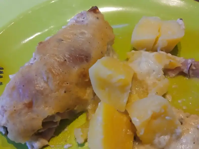Goudbruin gebakken kippenrolletjes met ham en aardappelen in room op een groen bord