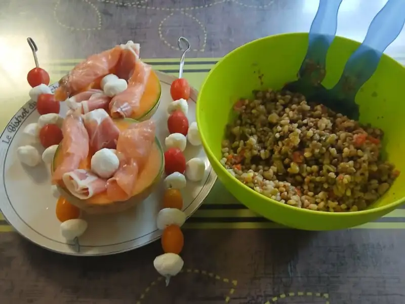 Halve meloenen gevuld met rauwe ham en mozzarellabolletjes, brochettes van kerstomaatjes en mozzarella, naast een slakom