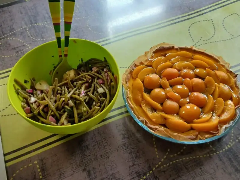 Taart met perziken en abrikozen op siroop in een rozet op bladerdeeg, naast een salade van sperziebonen