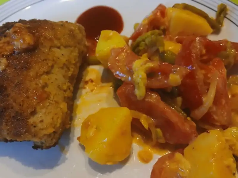 Goudbruine snee vleesbrood met gebakken aardappelen, tomaten en sperziebonen op een bord