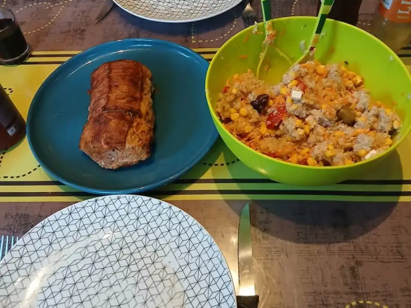 Goudbruin zalmgebraad uit de oven op een blauw bord naast een slaschaal rijstsalade met maïs, tomaten, feta en olijven